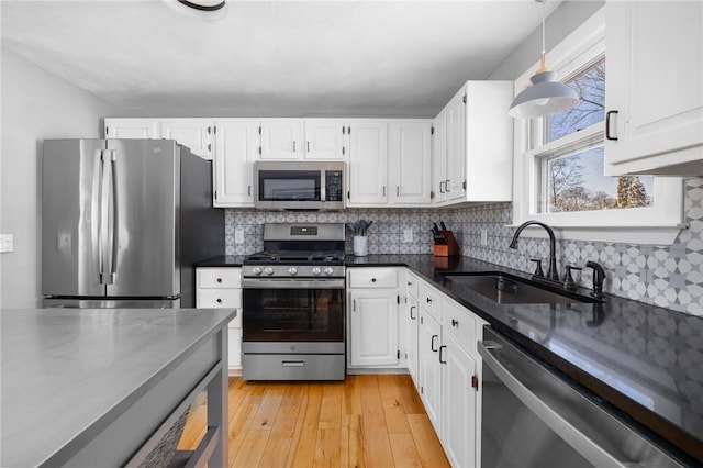 kitchen with white cabinetry, light hardwood / wood-style floors, appliances with stainless steel finishes, decorative light fixtures, and sink