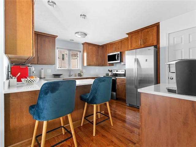 kitchen with dark wood-type flooring, appliances with stainless steel finishes, sink, and a breakfast bar area