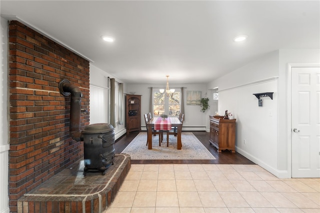 dining space featuring light tile patterned flooring, baseboard heating, a wood stove, and an inviting chandelier