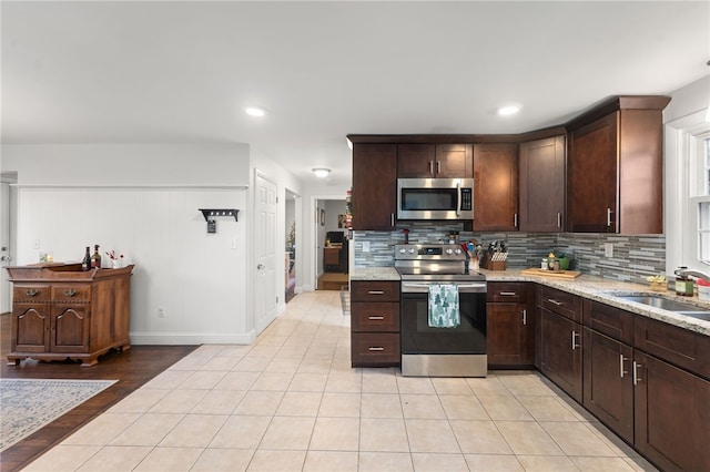 kitchen with tasteful backsplash, sink, light stone countertops, stainless steel appliances, and light tile patterned floors