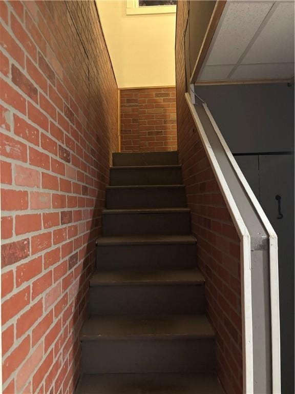 stairway with a paneled ceiling and brick wall