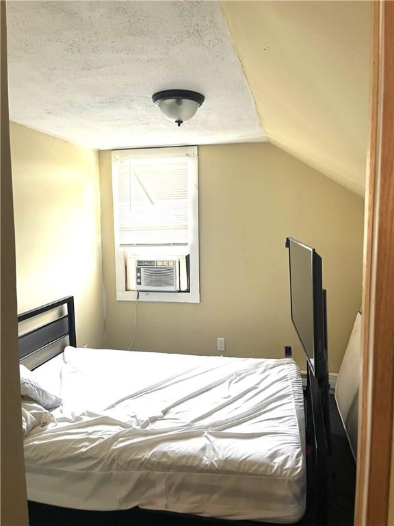 bedroom featuring lofted ceiling, cooling unit, and a textured ceiling