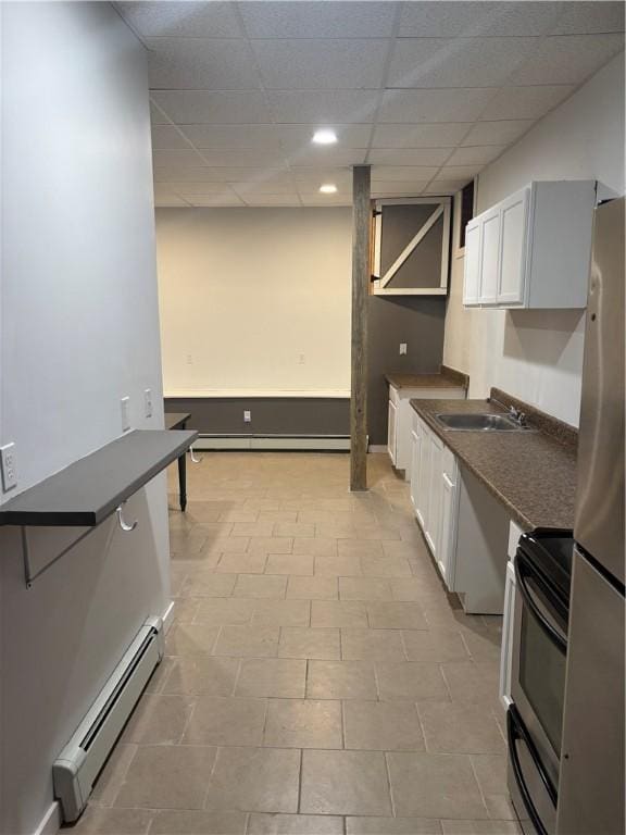 kitchen featuring a baseboard radiator, white cabinets, appliances with stainless steel finishes, sink, and a drop ceiling