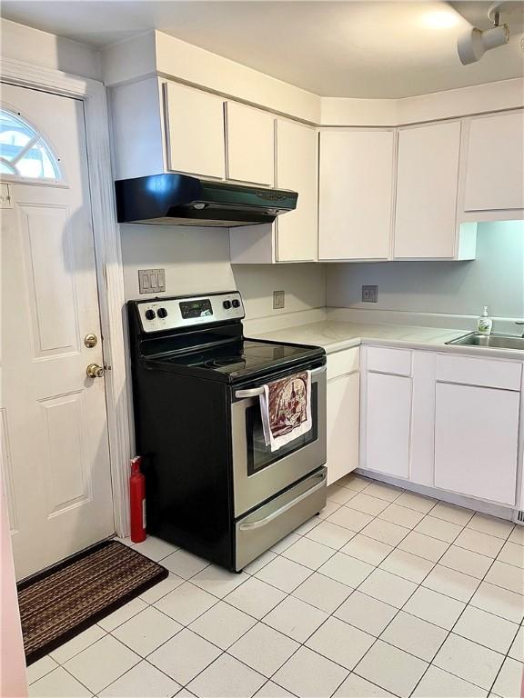 kitchen featuring sink, stainless steel electric range oven, light tile patterned flooring, and white cabinetry