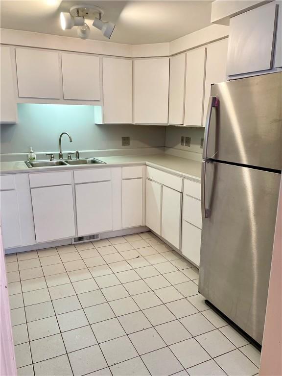 kitchen featuring sink, stainless steel refrigerator, white cabinetry, and light tile patterned flooring