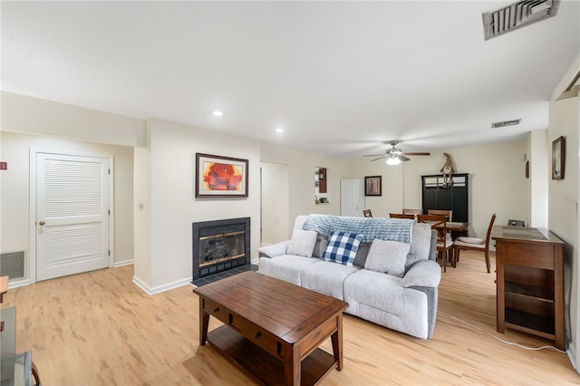 living room with ceiling fan, a tiled fireplace, and light hardwood / wood-style flooring