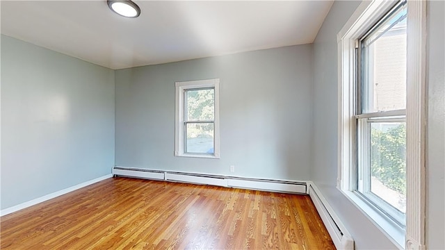 spare room with a baseboard heating unit, light wood-type flooring, and a wealth of natural light