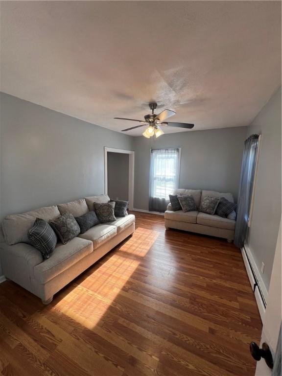 living room with dark wood-type flooring, ceiling fan, and baseboard heating