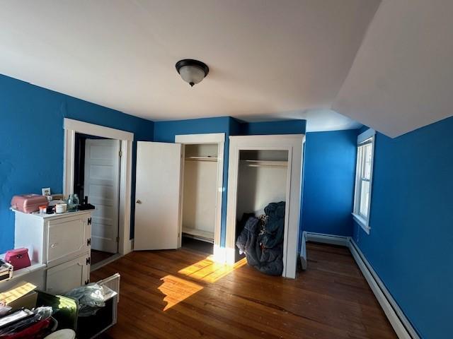 bedroom featuring multiple closets, vaulted ceiling, dark hardwood / wood-style flooring, and a baseboard radiator