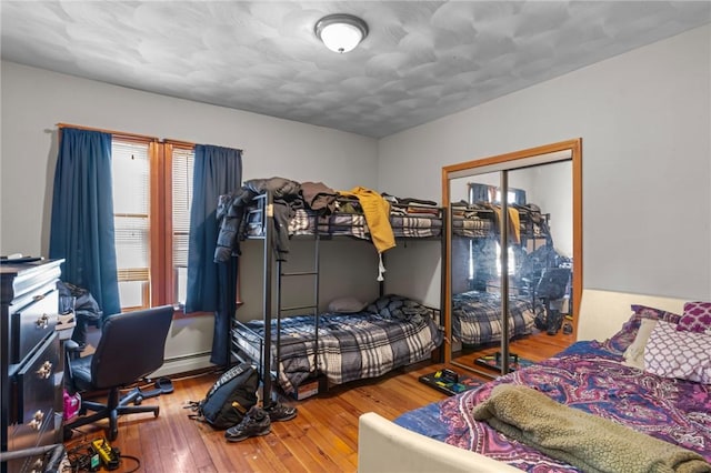 bedroom with baseboard heating, hardwood / wood-style floors, and a closet