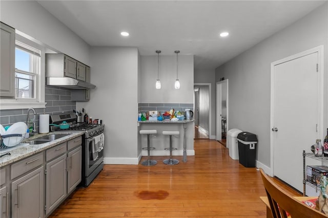 kitchen with gray cabinets, light hardwood / wood-style floors, decorative backsplash, sink, and stainless steel gas range