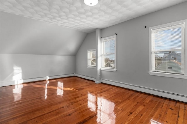 additional living space with a baseboard radiator, wood-type flooring, lofted ceiling, and a textured ceiling