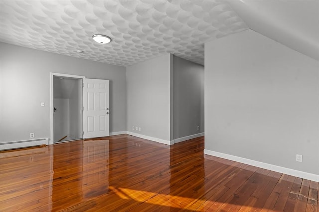 empty room featuring baseboard heating, vaulted ceiling, and hardwood / wood-style floors