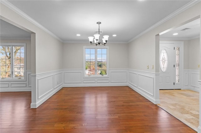 unfurnished dining area featuring hardwood / wood-style flooring, crown molding, and a notable chandelier