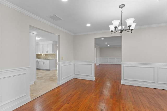 unfurnished dining area with an inviting chandelier, crown molding, and light hardwood / wood-style floors