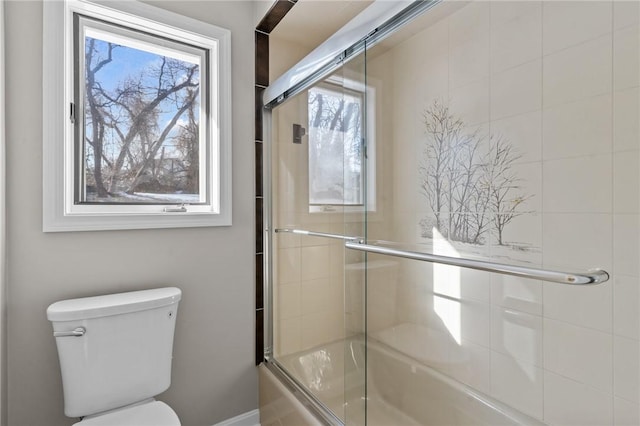 bathroom featuring toilet and shower / bath combination with glass door