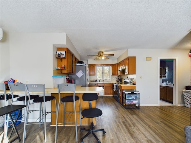 kitchen featuring a breakfast bar, sink, stainless steel range with electric cooktop, dark hardwood / wood-style floors, and kitchen peninsula