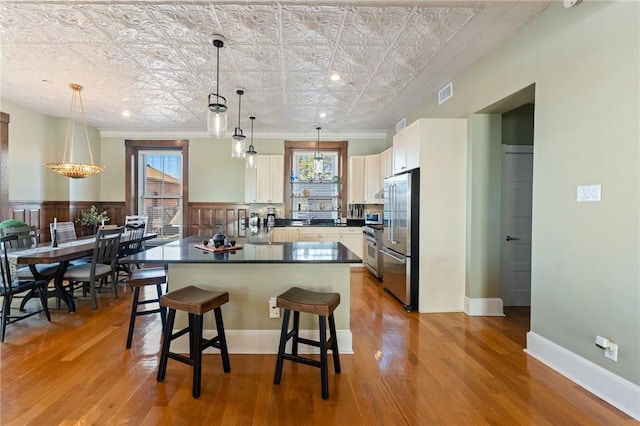 kitchen featuring pendant lighting, high quality appliances, white cabinetry, a breakfast bar, and light hardwood / wood-style floors