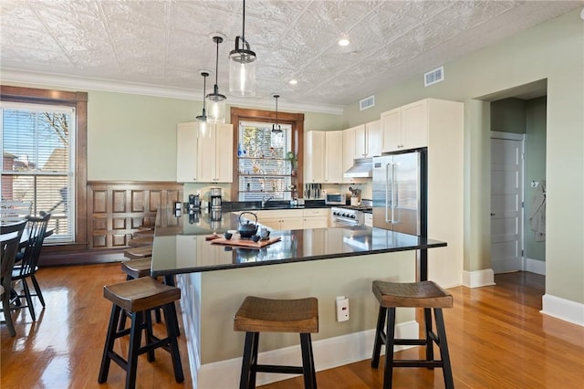 kitchen with high quality appliances, wood-type flooring, pendant lighting, and a breakfast bar