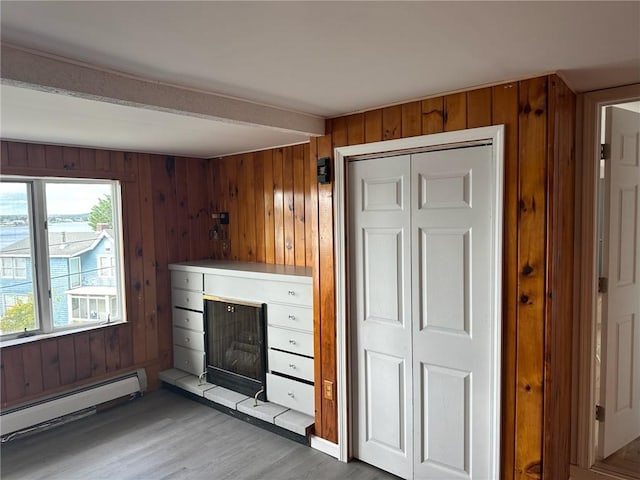 unfurnished living room with hardwood / wood-style flooring, wooden walls, and a baseboard heating unit