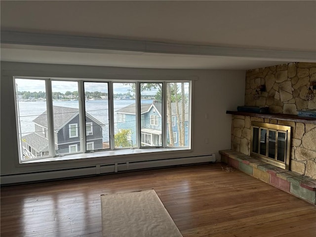 unfurnished living room featuring baseboard heating, a wealth of natural light, and a stone fireplace