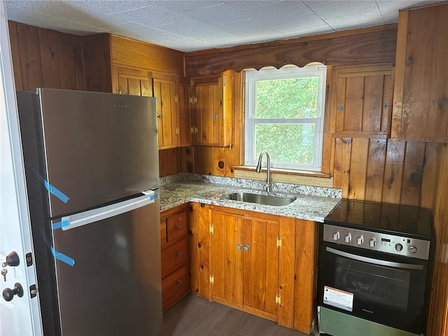 kitchen with sink, dark wood-type flooring, light stone countertops, wooden walls, and stainless steel appliances