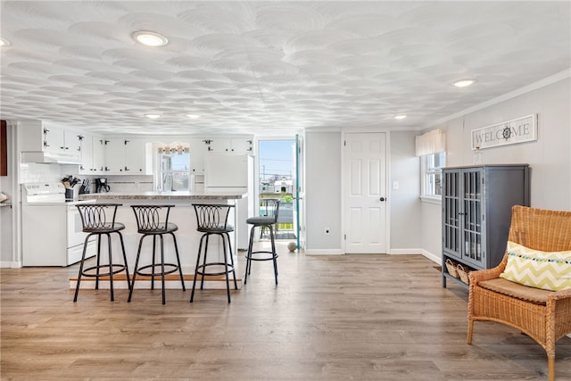 kitchen featuring kitchen peninsula, crown molding, light hardwood / wood-style flooring, white cabinets, and white appliances