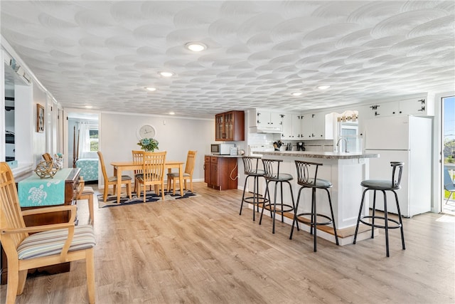 kitchen featuring light stone countertops, white cabinets, white fridge, sink, and light wood-type flooring