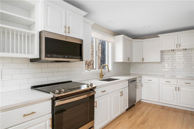 kitchen with appliances with stainless steel finishes, sink, white cabinets, and light hardwood / wood-style flooring