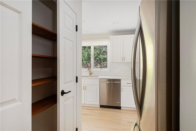 kitchen with sink, white cabinets, decorative backsplash, stainless steel appliances, and light hardwood / wood-style flooring