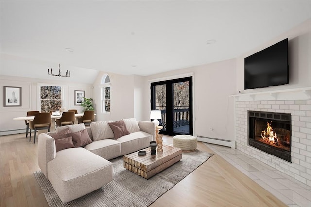 living room with an inviting chandelier, vaulted ceiling, a brick fireplace, light hardwood / wood-style flooring, and baseboard heating