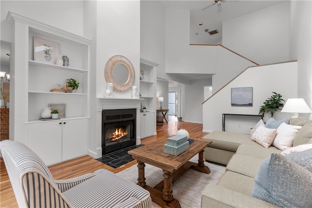 living room with built in shelves, light wood-type flooring, and a towering ceiling