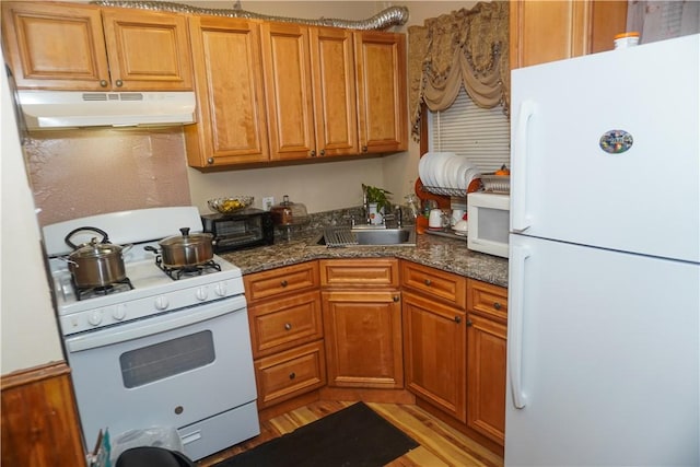 kitchen with white appliances, dark stone counters, sink, and light hardwood / wood-style flooring