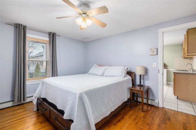 bedroom featuring ceiling fan, light hardwood / wood-style floors, sink, and a baseboard heating unit