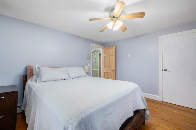 bedroom featuring hardwood / wood-style flooring, a baseboard heating unit, and ceiling fan