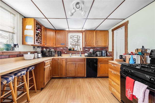 kitchen with black appliances, sink, backsplash, light wood-type flooring, and a drop ceiling