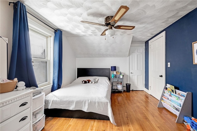 bedroom with ceiling fan, light hardwood / wood-style floors, and lofted ceiling