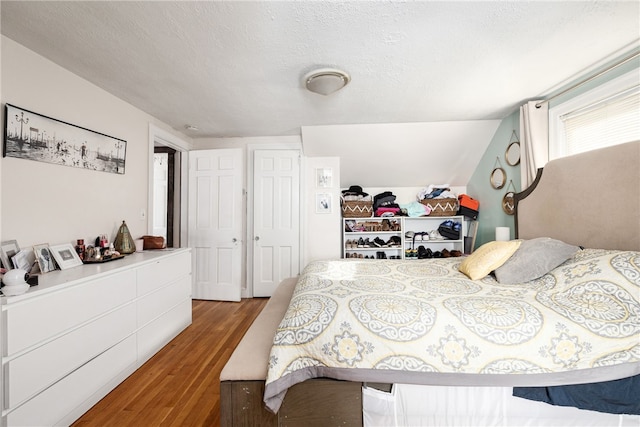 bedroom featuring hardwood / wood-style floors, a textured ceiling, and vaulted ceiling