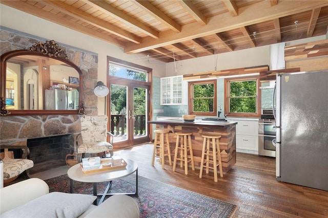 living room featuring wood-type flooring, a stone fireplace, sink, wooden ceiling, and beam ceiling