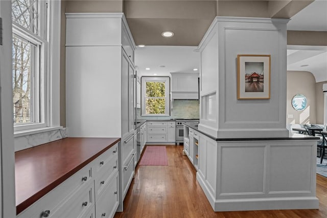 kitchen with light hardwood / wood-style flooring, appliances with stainless steel finishes, white cabinetry, tasteful backsplash, and exhaust hood