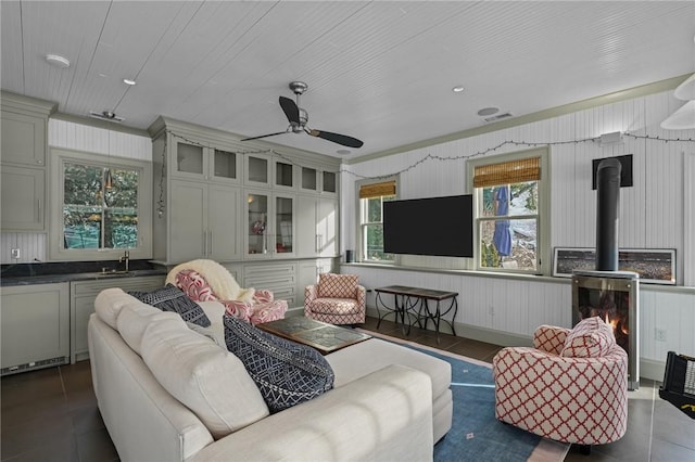 tiled living room with ceiling fan, sink, and a wood stove