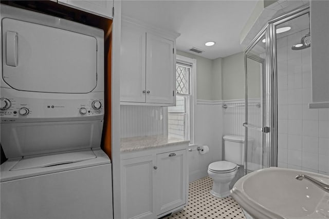 bathroom featuring stacked washer and dryer, a shower with shower door, and toilet