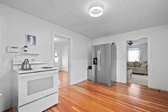 kitchen with light wood-type flooring, a textured ceiling, stainless steel fridge, and electric stove