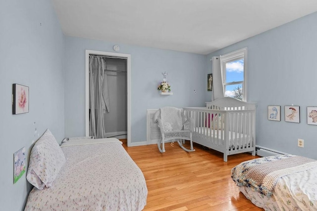 bedroom with wood-type flooring, baseboard heating, and a closet