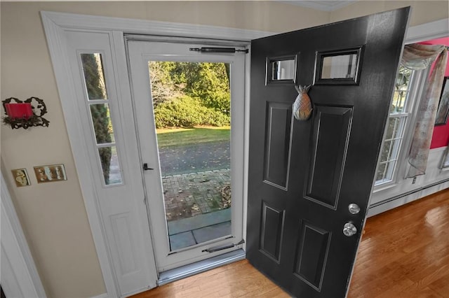 doorway to outside with a baseboard heating unit, ornamental molding, and light wood-type flooring