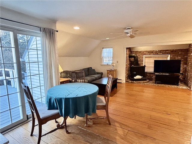 dining room featuring ceiling fan, light hardwood / wood-style floors, a baseboard radiator, a wood stove, and vaulted ceiling