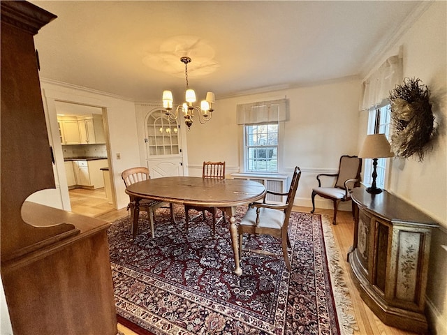 dining area with light wood-type flooring, crown molding, and a notable chandelier