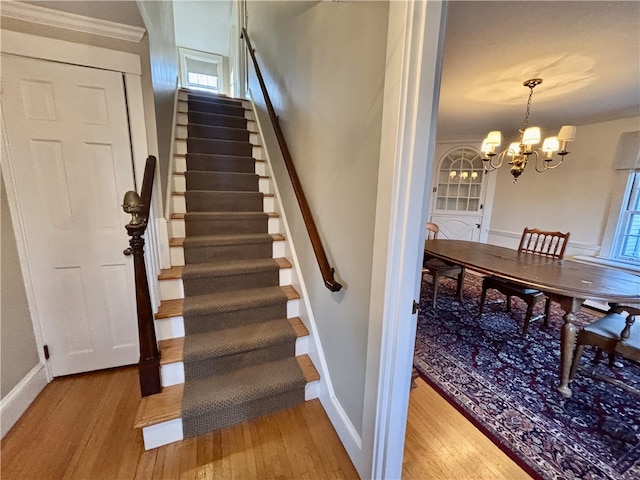 stairs with a chandelier, crown molding, and wood-type flooring