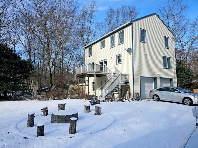 snow covered property featuring a garage, an outdoor fire pit, and a wooden deck