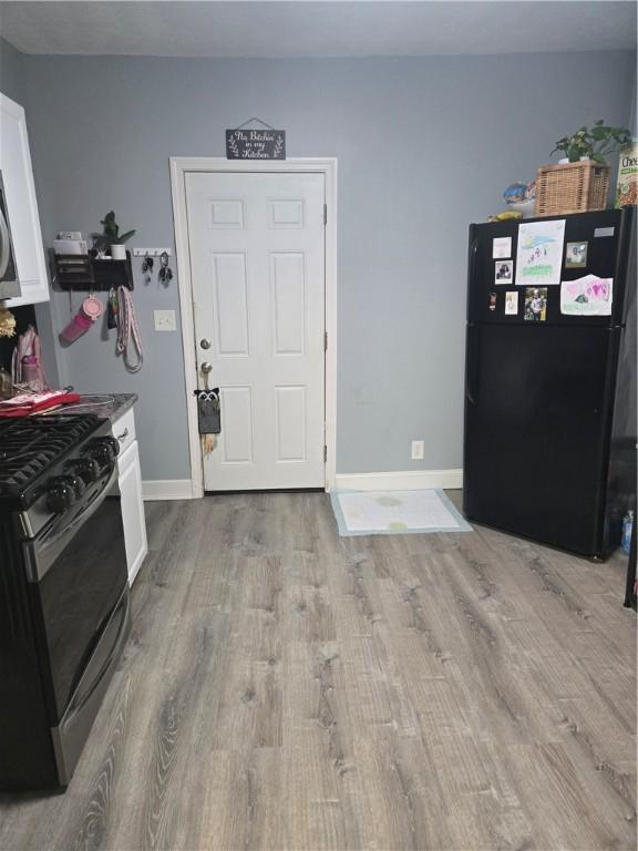 interior space with black refrigerator, light hardwood / wood-style flooring, white cabinets, and stainless steel gas range